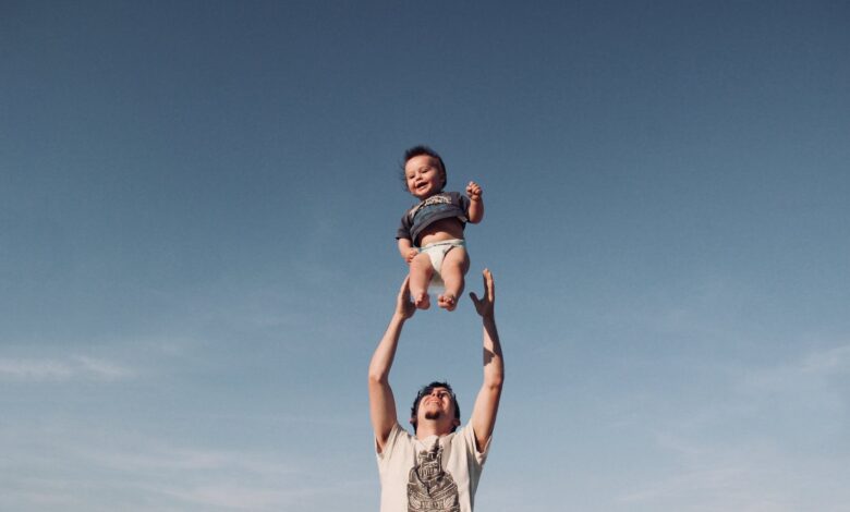 photo of a man raising baby under blue sky